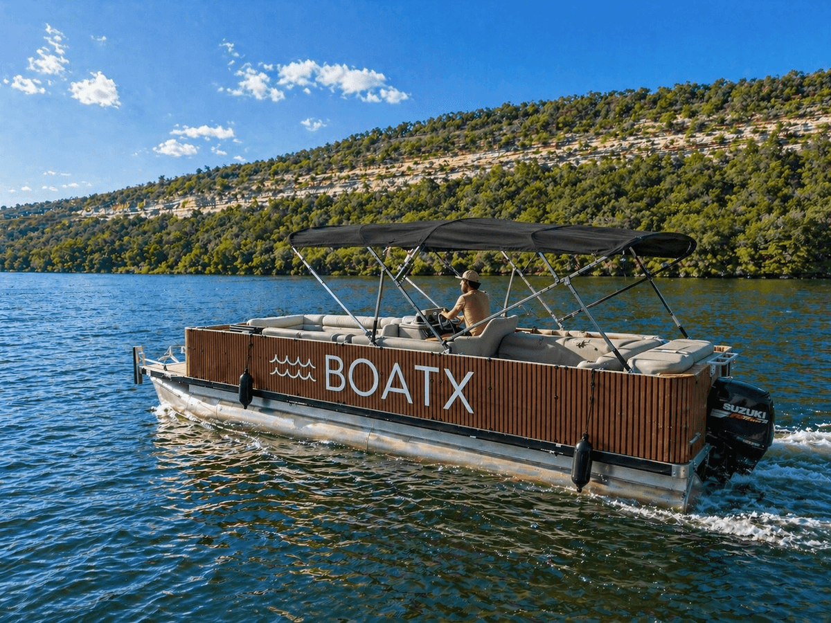 The Tiki BOATX teak wood-wrapped pontoon boat cruising on Lake Austin with captain and Hill Country shoreline
